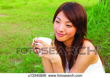 Stock Photograph - Young woman sitting, holding a cup. Fotosearch