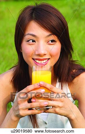 Young woman sitting, holding glass of orange juice View Large Photo Image Stock Image - Young woman sitting, holding glass of orange juice. Fotosearch