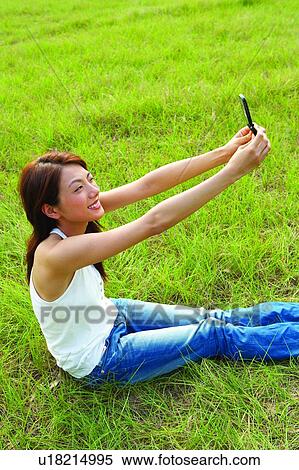 Young woman sitting on grass, holding mobile phone, cheerful View Large Photo Image Stock Photography - Young woman sitting on grass, holding mobile phone, cheerful. Fotosearch