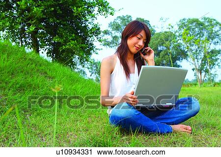 Young woman sitting on grass, using mobile phone and notebook computer View Large Photo Image Stock Image - Young woman sitting on grass, using mobile phone and notebook computer. Fotosearch