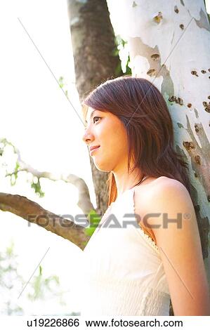 Young woman standing and leaning to tree View Large Photo Image Stock Photograph - Young woman standing and leaning to tree. Fotosearch