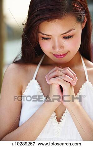 Stock Photo - Young woman standing head down praying. Fotosearch