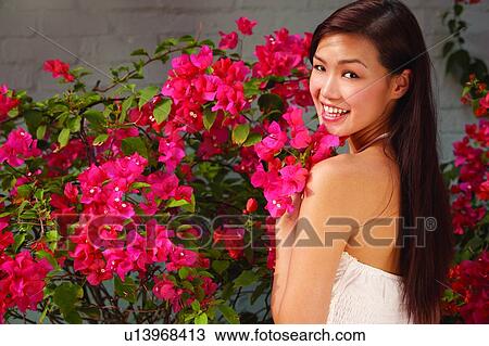 Young woman standing near flower, turning back and smiling, close up View Large Photo Image Stock Image - Young woman standing near flower, turning back and smiling, close up. Fotosearch