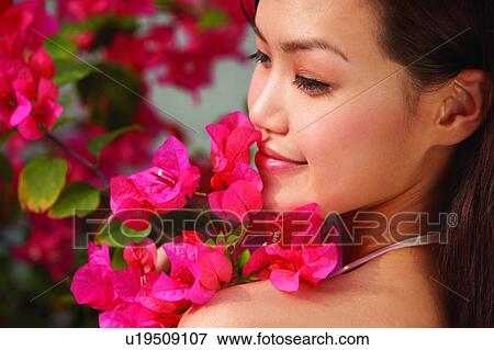 Stock Photo - Young woman standing near flower, turning back and smiling, close up. Fotosearch