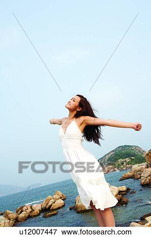 Stock Photo - Young woman standing near the sea, stretching out. Fotosearch