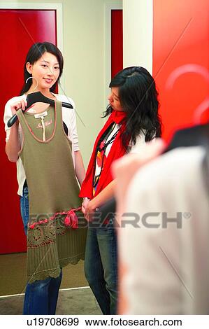 Stock Photo - Young woman holding clothes, seeking for advice. Fotosearch