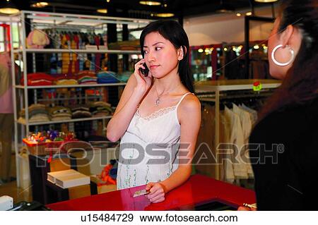Stock Photo - Young woman holding credit card, using mobile phone. Fotosearch