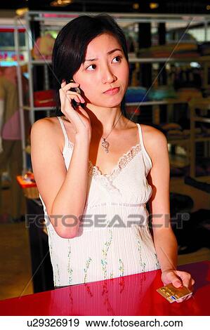 Stock Photo - Young woman holding credit card, using mobile phone. Fotosearch