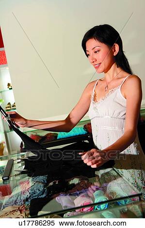 Stock Photography - Young woman shopping at boutique, standing, holding and looking at a clothes. Fotosearch