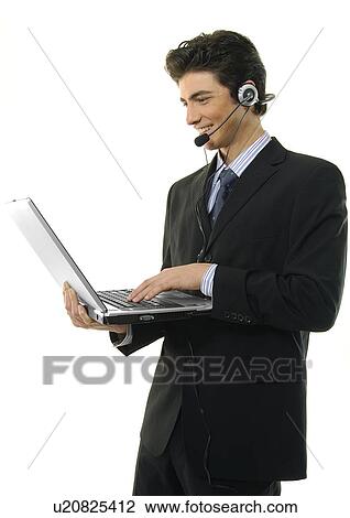 Stock Image - Side profile of a businessman wearing a headset and using a laptop. Fotosearch