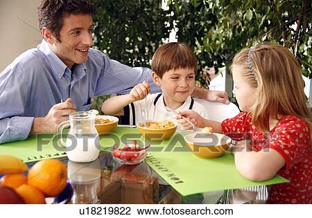 Stock Image - Father and children eating breakfast. Fotosearch