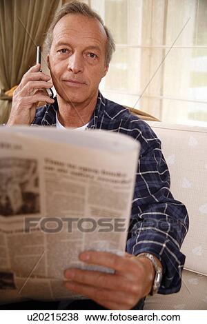 Stock Photo - Mature man reading newspaper and talking on cell phone. Fotosearch