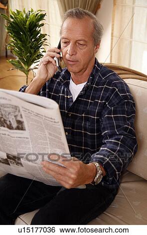 Stock Photograph - Mature man reading newspaper and talking on cell phone. Fotosearch