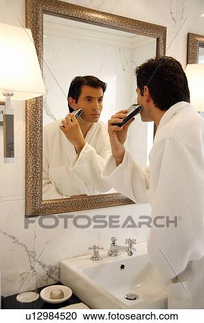Stock Image - Man shaving in the bathroom mirror. Fotosearch