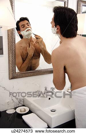Stock Image - Man shaving in the bathroom mirror. Fotosearch
