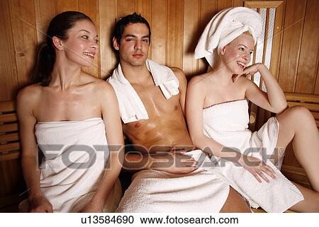 Stock Image - Man with two young women enjoying a sauna. Fotosearch