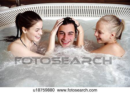 Stock Image - One man with two women in jacuzzi at a spa. Fotosearch