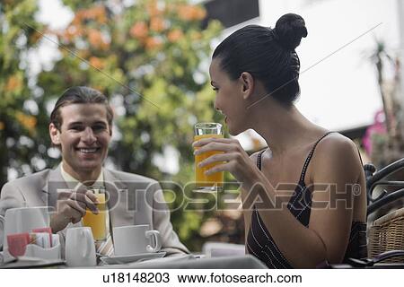 Stock Image - Business couple in garden cafe drinking orange juice. Fotosearch