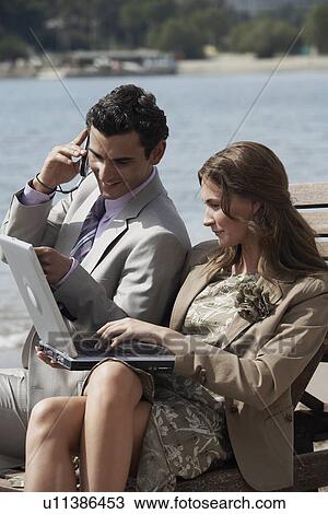 Stock Image - Business couple on beach with cell phone and laptop. Fotosearch