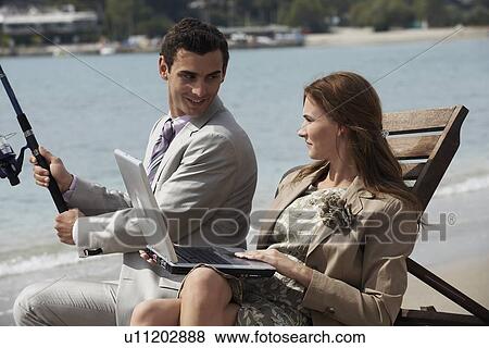Business couple on beach with fishing rod and laptop View Large Photo Image Stock Photo - Business couple on beach with fishing rod and laptop. Fotosearch
