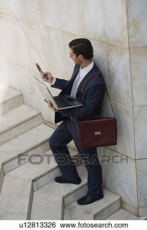 Stock Photograph - Businessman holding laptop and cell phone. Fotosearch