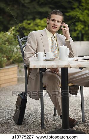 Stock Photo - Businessman in garden cafe with cell phone. Fotosearch