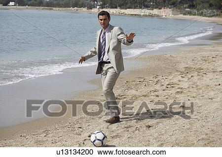 Stock Image - Businessman on beach playing soccer. Fotosearch