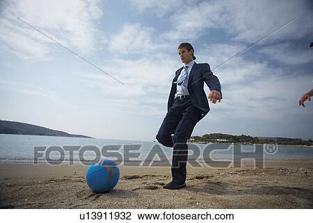 Stock Image - Businessman on beach with globe beach ball. Fotosearch
