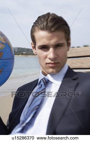 Stock Image - Businessman on beach with globe beach ball. Fotosearch