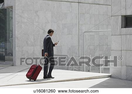 Stock Image - Businessman walking with a suitcase and cell phone. Fotosearch