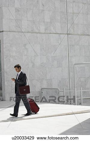 Stock Photo - Businessman walking with a suitcase and cell phone. Fotosearch