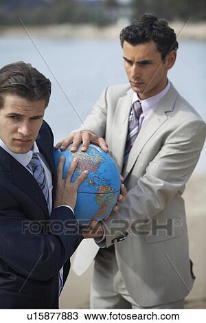 Stock Image - Businessmen on beach holding globe. Fotosearch