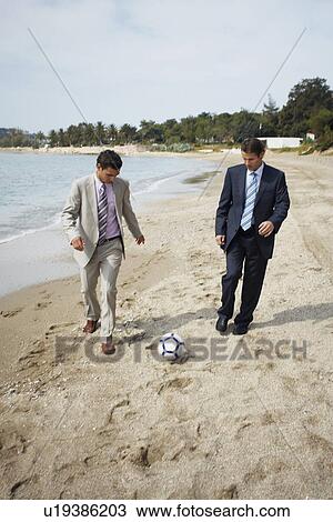 Stock Image - Businessmen on beach playing soccer. Fotosearch