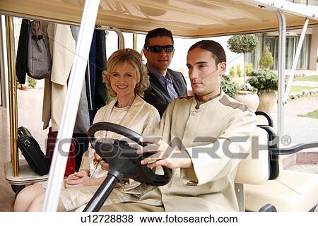 Stock Photo - Couple being driven in cart by hotel bellboy. Fotosearch