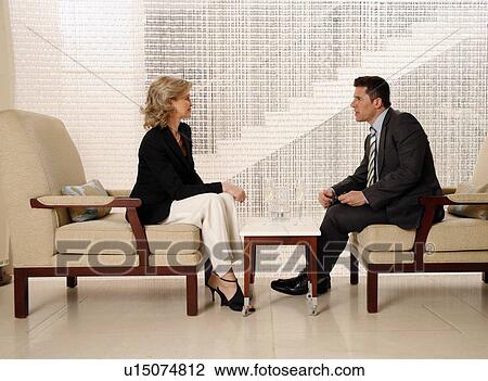 Stock Image - Man and woman sitting in hotel lobby. Fotosearch