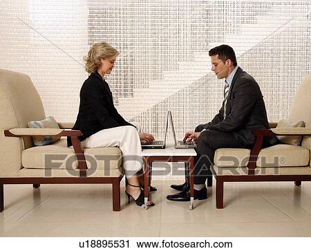 Stock Image - Man and woman sitting in hotel lobby. Fotosearch