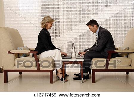 Stock Photo - Man and woman sitting in hotel lobby. Fotosearch