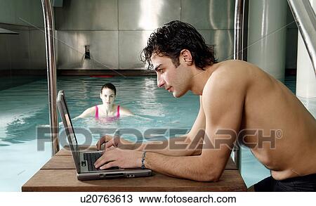 Stock Image - Man on computer nex t to a swimming pool. Fotosearch