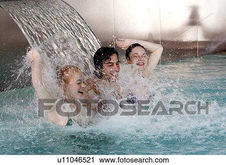 Stock Image - Young people standing under water spray in spa pool. Fotosearch