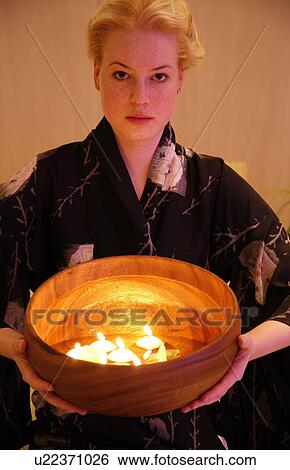 Stock Photograph - Young woman holding wooden bowl with burning candles. Fotosearch