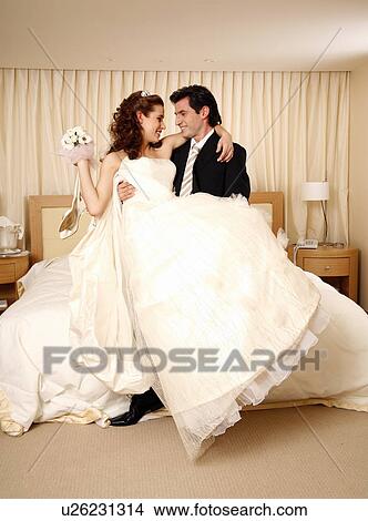 Picture - Groom holding bride in his arms in hotel room. Fotosearch