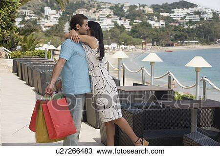 Stock Image - Woman embracing man holding shopping bags. Fotosearch