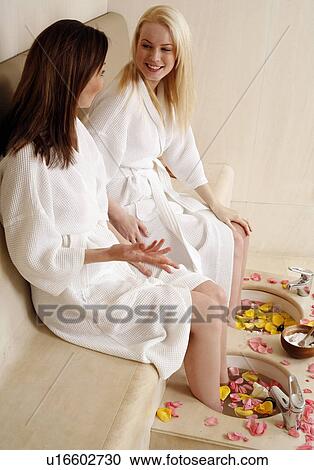 Stock Image - Two young women enjoying a foot bath with rose petals. Fotosearch