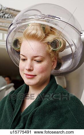 Stock Image - Young woman sitting under hairdryer. Fotosearch