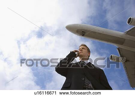 A Businessman Talking on a Cell Phone with an Airplane in the Background, Low Angle View, Waist Up View Large Photo Image Stock Image - A Businessman Talking on a Cell Phone with an Airplane in the Background, Low Angle View, Waist Up. Fotosearch