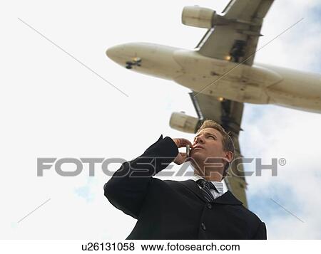 A Businessman Talking on a Cell Phone with an Airplane in the Background, Low Angle View, Waist Up View Large Photo Image Stock Photo - A Businessman Talking on a Cell Phone with an Airplane in the Background, Low Angle View, Waist Up. Fotosearch