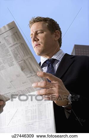 Stock Photo - A Mid Adult Businessman Reading a Newspaper, Low Angle View, Waist Up. Fotosearch