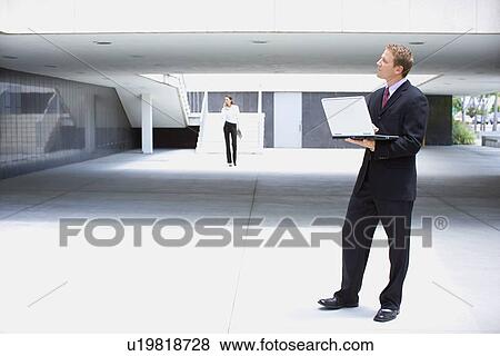 Stock Photo - A Mid Adult Businessman Using a Notebook Computer, Full Length. Fotosearch