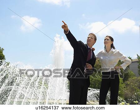 Stock Photo - A Pair of Office Workers by a Fountain, Looking Away, Three Quarter Length. Fotosearch
