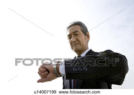 A Senior Adult Man Checking the Time with His Watch, Low Angle View View Large Photo Image Stock Photo - A Senior Adult Man Checking the Time with His Watch, Low Angle View. Fotosearch